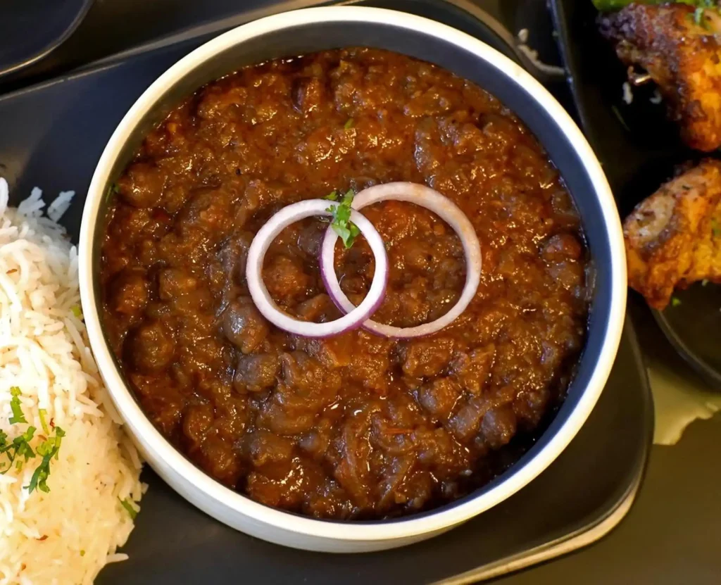 Channa Masala made with tender chickpeas simmered in a rich tomato and onion gravy, garnished with red onion rings and fresh cilantro.