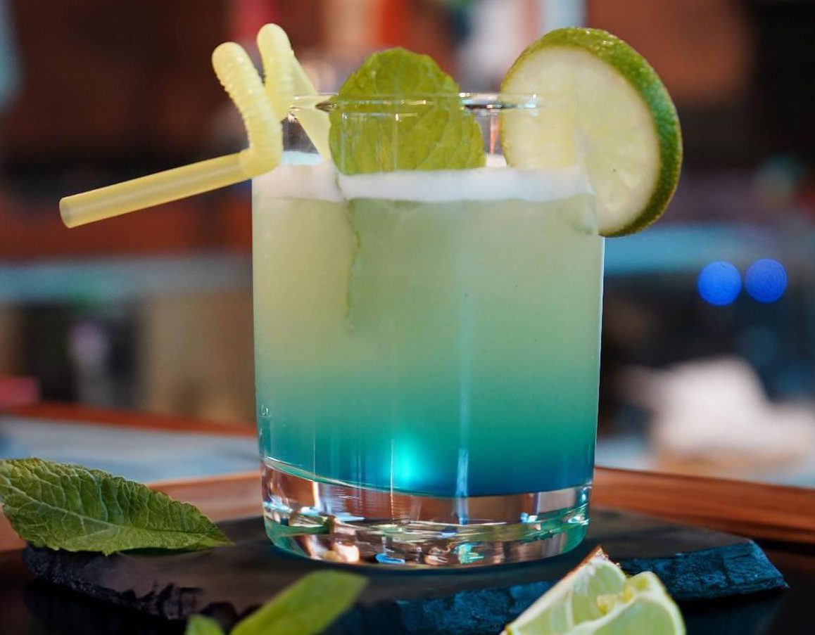 Blue mocktail served over ice with fresh lime slices, mint leaves, and a lemon garnish at Bombay Kitchen & Bar.